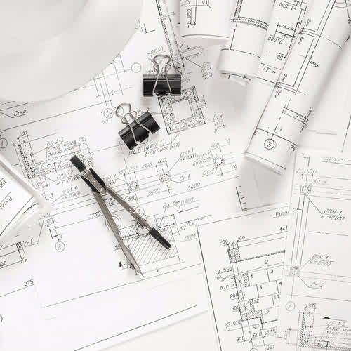 Planos técnicos de obra con casco y compás sobre la mesa de trabajo