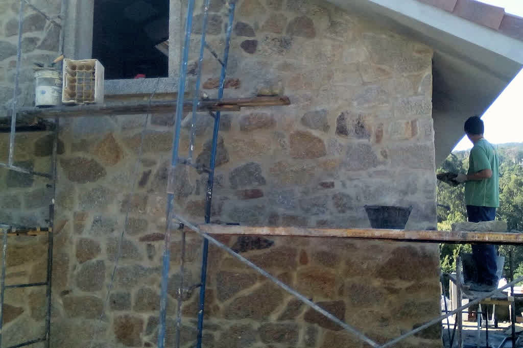 Albañil trabajando en la fachada de piedra de una casa en el Val Miñor